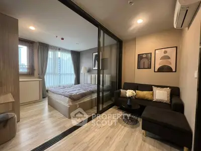 Modern studio apartment with cozy living area and stylish bedroom separated by glass partition.