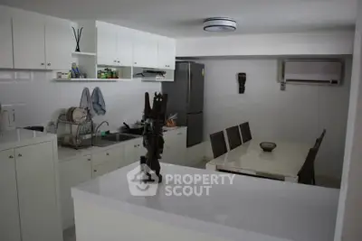 Modern kitchen with dining area, featuring sleek white cabinets and stainless steel appliances.