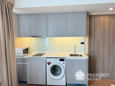 Modern kitchen with sleek cabinets, washing machine, and microwave in compact layout.