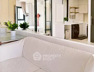 Modern living room with cozy white sofa and sleek kitchen featuring washing machine and stylish decor.