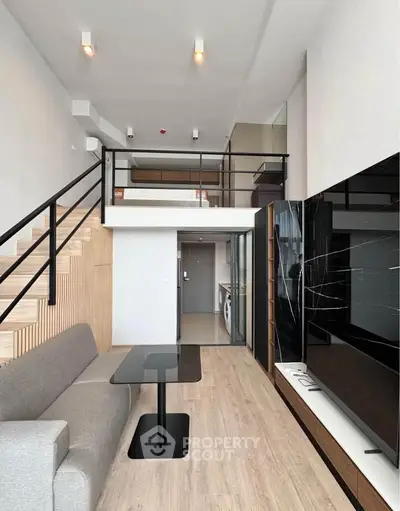 Modern duplex living room with sleek design and staircase, featuring a cozy sofa and stylish decor.