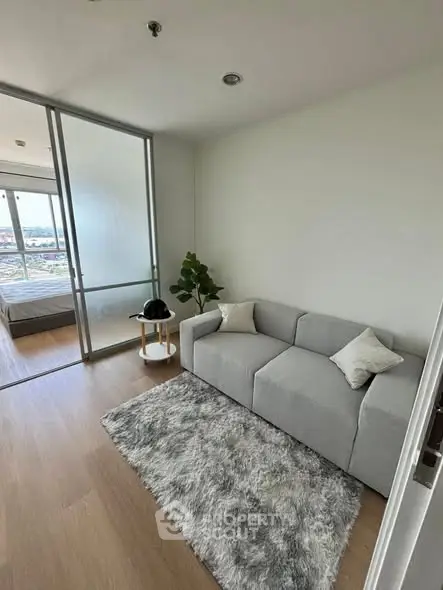 Modern living room with cozy gray sofa and plush rug, featuring a view into a stylish bedroom.