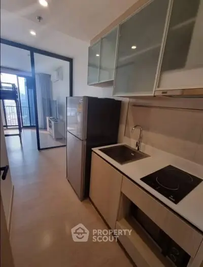Modern kitchen with sleek design, featuring induction cooktop and stainless steel fridge, leading to a bright living area.