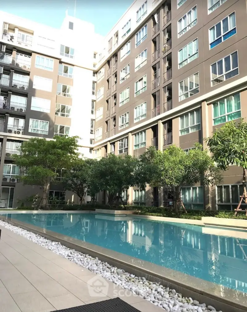 Modern apartment building with pool and lush greenery in urban setting.