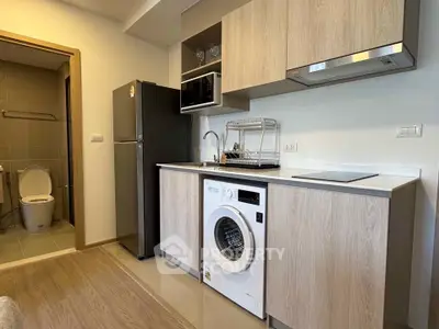 Modern kitchen with washing machine and sleek cabinetry in compact apartment.