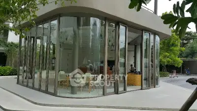 Modern glass-walled building with stylish interior seating and lush greenery.