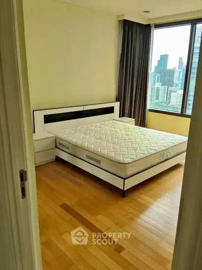 Spacious bedroom with city view and modern furnishings in high-rise apartment.