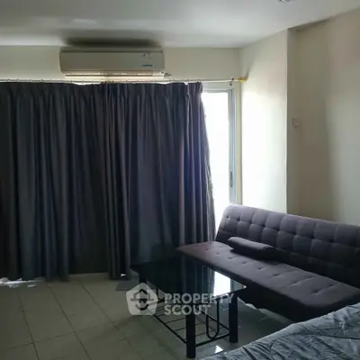 Cozy living room with modern sofa and glass coffee table, featuring large window with curtains and air conditioning.