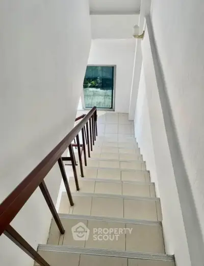 Modern staircase with sleek wooden railing and tiled steps in bright interior.