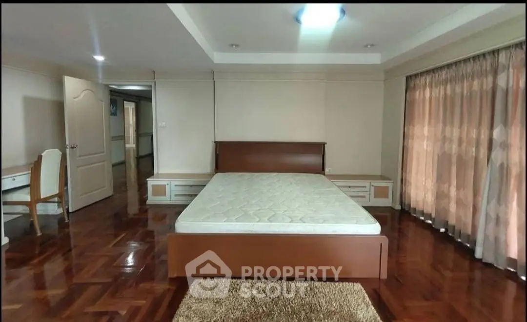 Spacious bedroom with wooden flooring and large windows for natural light.