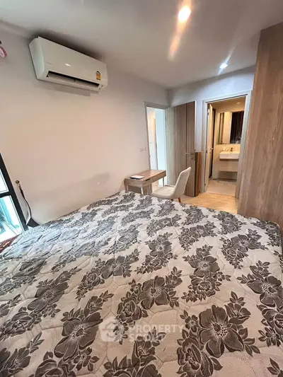 Cozy bedroom with floral bedding and air conditioning, featuring a small desk and chair near the window.