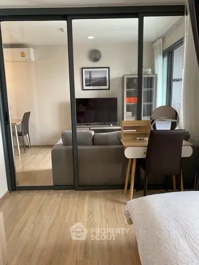 Modern living room with glass partition, stylish furniture, and wooden flooring in a cozy apartment.