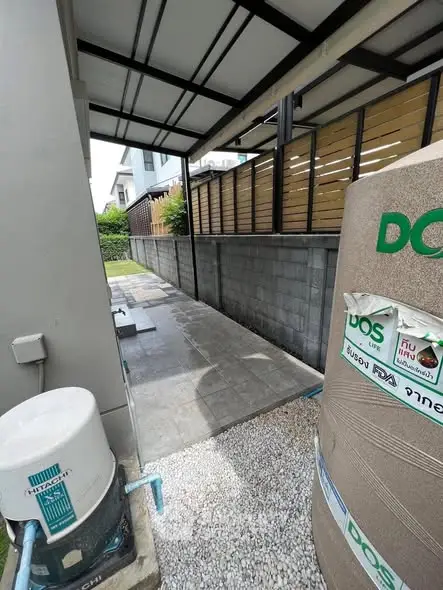 Modern exterior walkway with covered roof and garden view, featuring utility equipment.