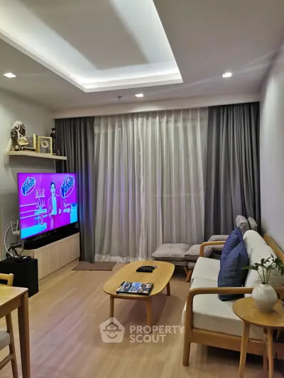 Modern living room with cozy seating and large TV, featuring elegant curtains and stylish decor.