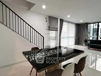 Modern dining area with sleek table and staircase in stylish open-plan living space.