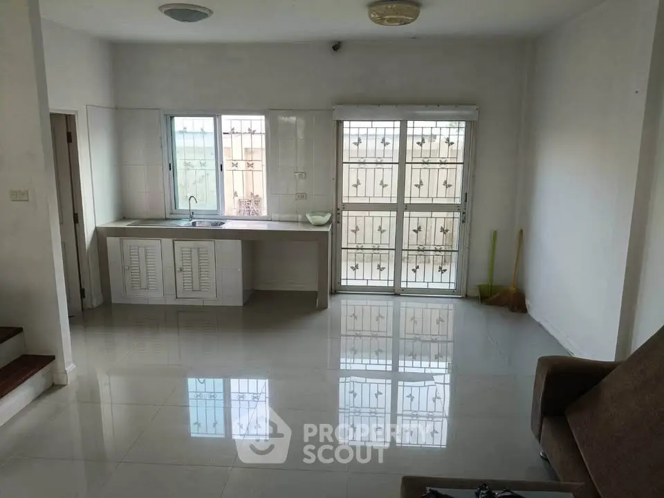 Spacious living area with sleek tiled flooring and natural light, featuring a minimalist kitchen setup.