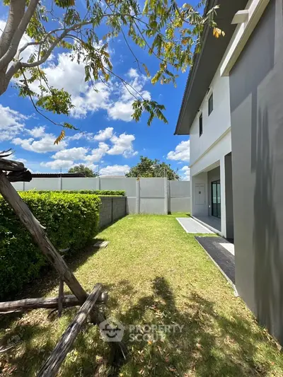 Spacious backyard with lush greenery and modern exterior under a clear blue sky.