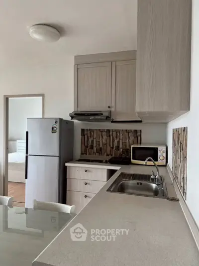 Modern kitchen with sleek cabinetry, stainless steel fridge, and cozy dining area in a stylish apartment.