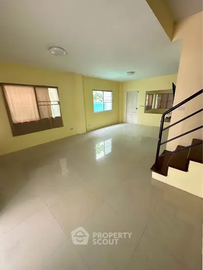 Spacious unfurnished living room with large windows and staircase, perfect for customization.