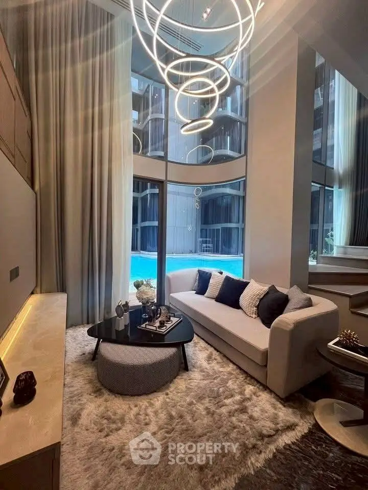 Luxurious living room with modern chandelier and pool view, featuring elegant decor and high ceilings.