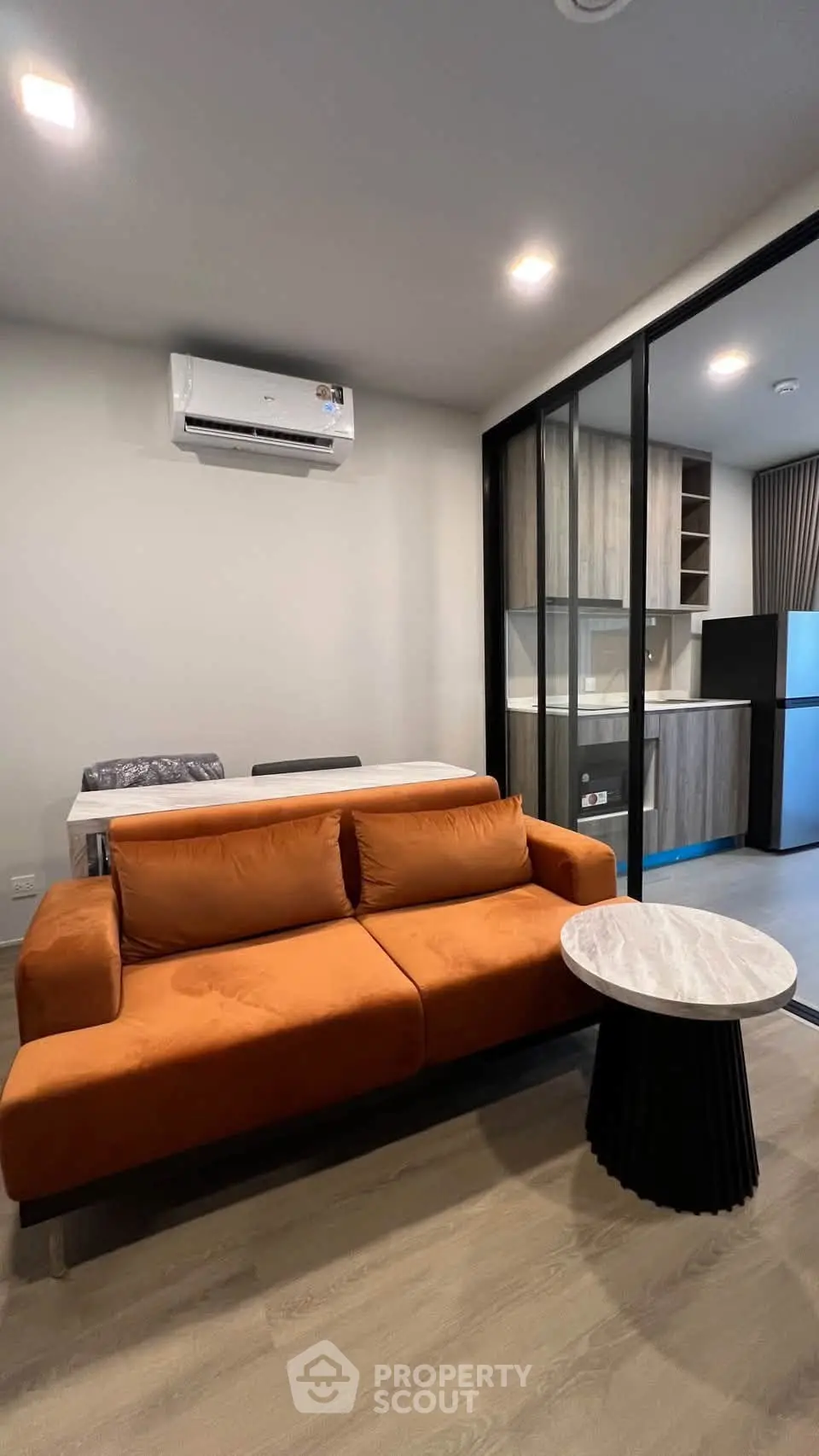Modern living room with orange sofa, marble table, and sleek kitchen in open layout apartment.