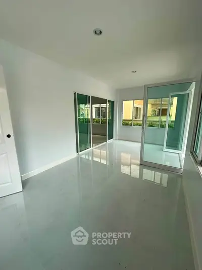 Spacious sunlit room with large windows and glossy floors, perfect for modern living.