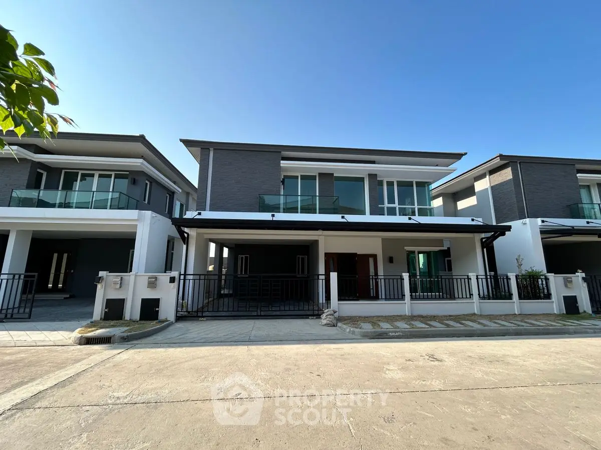 Modern two-story house with sleek design and spacious balcony under clear blue sky.