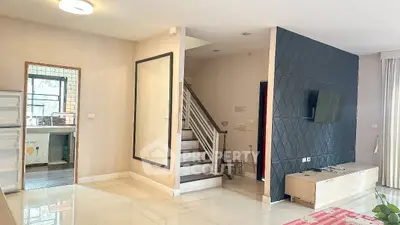 Modern living room with staircase and wall-mounted TV, open layout leading to kitchen.