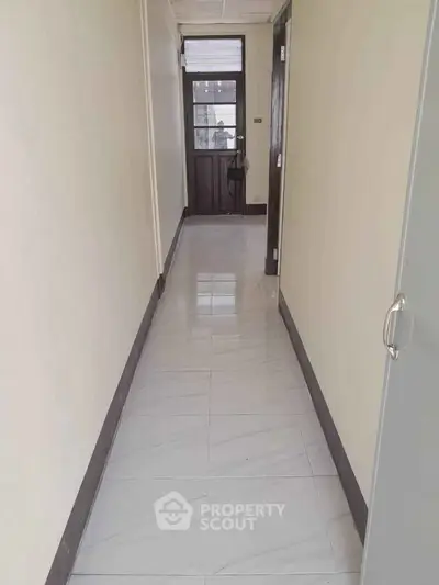 Bright corridor with tiled flooring leading to a glass door, ideal for natural light entry.