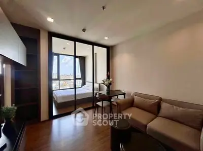 Modern living room with cozy sofa and glass partition leading to a bright bedroom with city view.