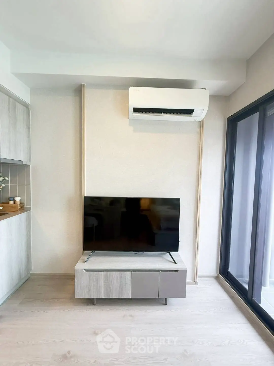 Modern living room with sleek TV setup and air conditioning, featuring large windows for natural light.