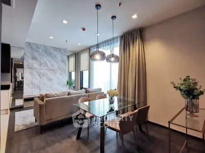 Modern living room with elegant glass dining table and cozy seating area, featuring stylish lighting and floor-to-ceiling windows.