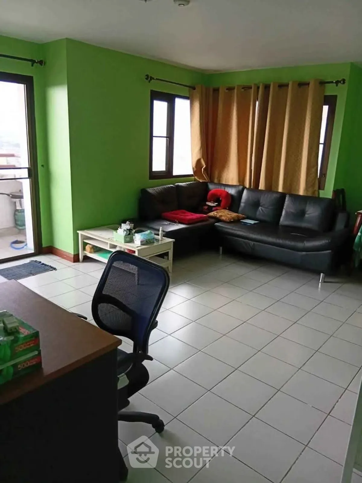 Spacious living room with green walls, black leather sofa, and office chair, perfect for relaxation and work.