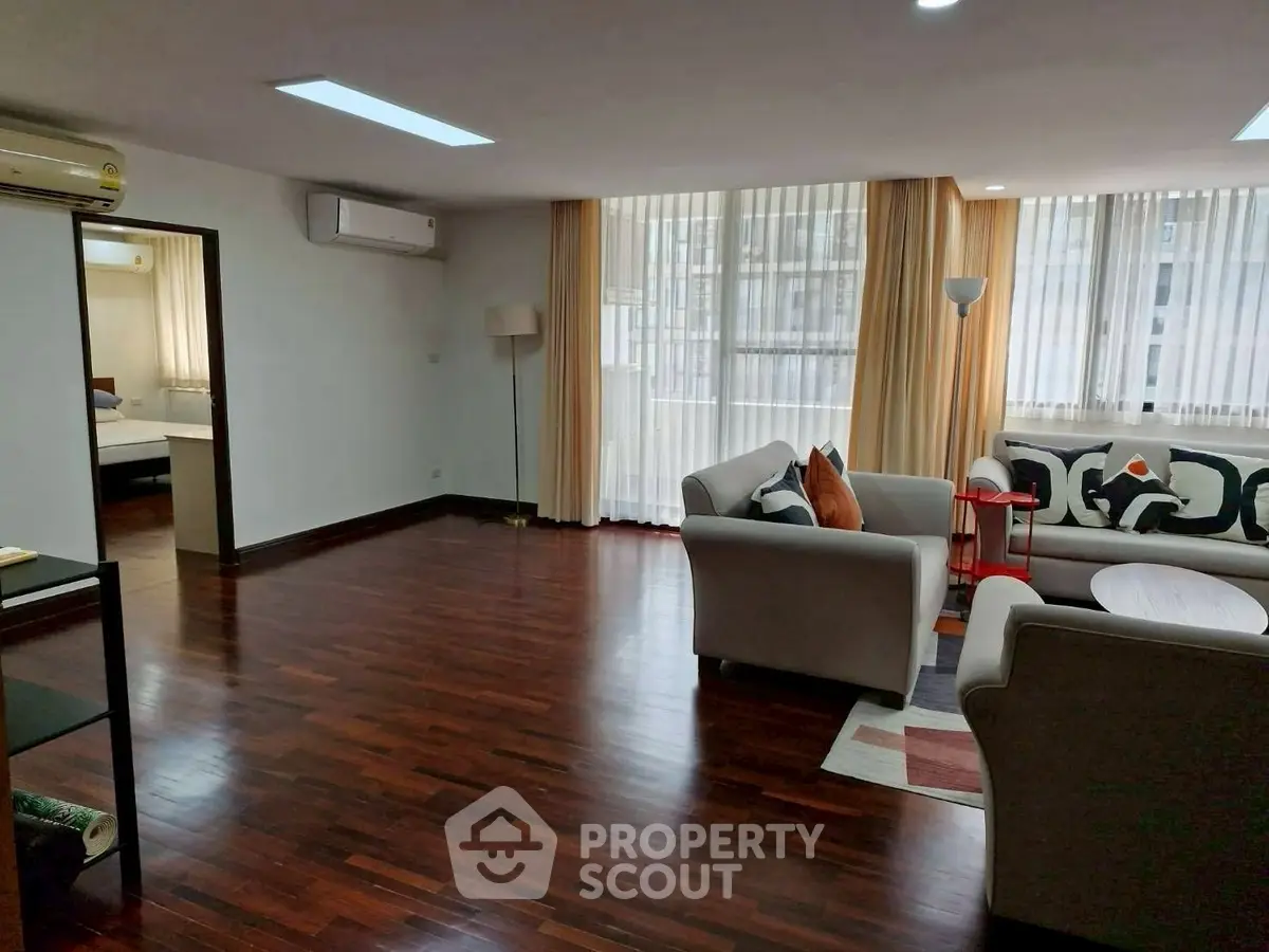 Spacious living room with hardwood floors and modern furniture in a bright apartment.