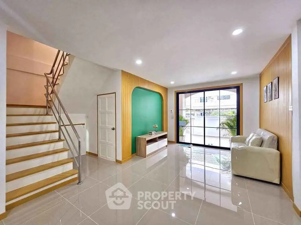 Spacious modern living room with sleek staircase and large window view.