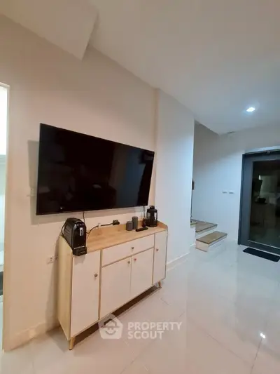 Modern living room with wall-mounted TV and sleek cabinet, showcasing minimalist design and bright lighting.