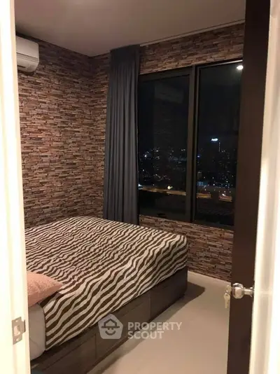 Cozy bedroom with city view, featuring stylish brick accent wall and modern furnishings.