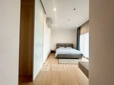 Spacious modern bedroom with wooden flooring and large windows for natural light.