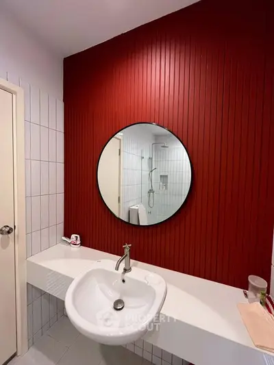 Modern bathroom with red accent wall and round mirror