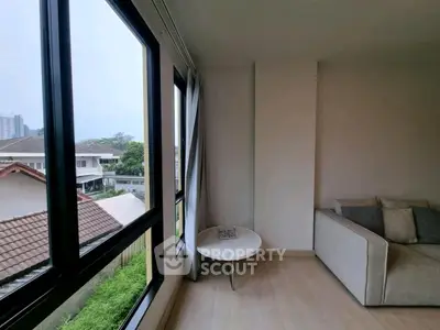 Cozy living room with large windows and modern sofa, offering a serene view of the neighborhood.