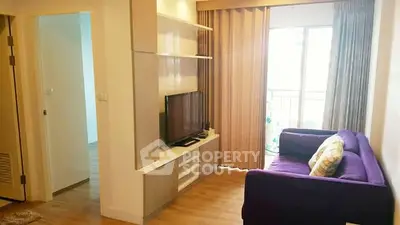 Cozy living room with purple sofa and TV, leading to a bright balcony.