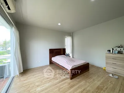 Spacious bedroom with wooden flooring and large window offering natural light and garden view.