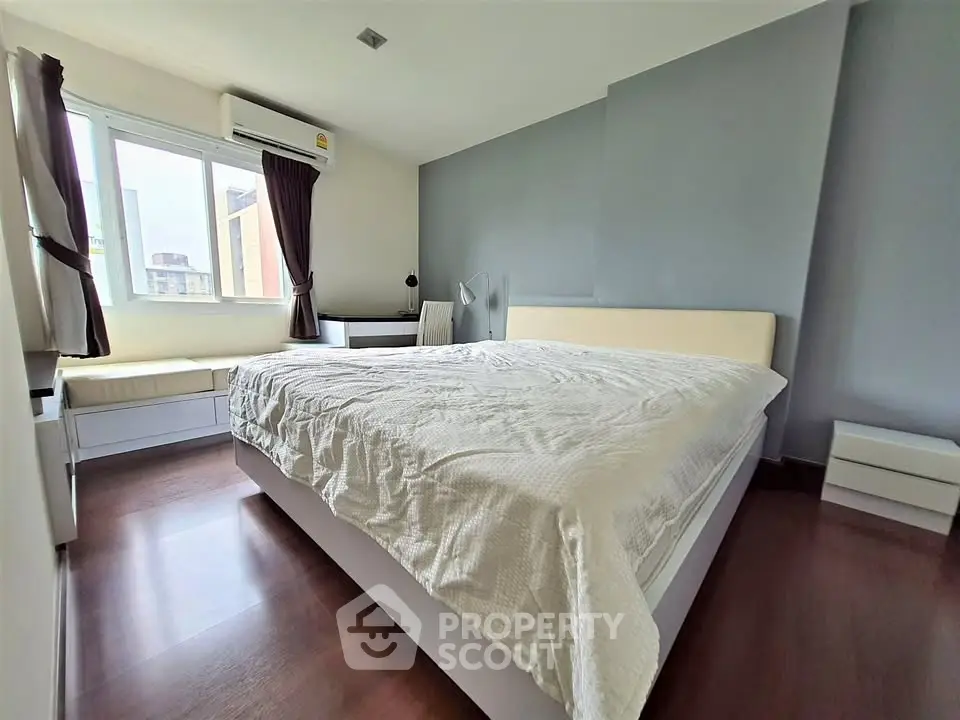Spacious bedroom with large window and modern furnishings in a stylish apartment.