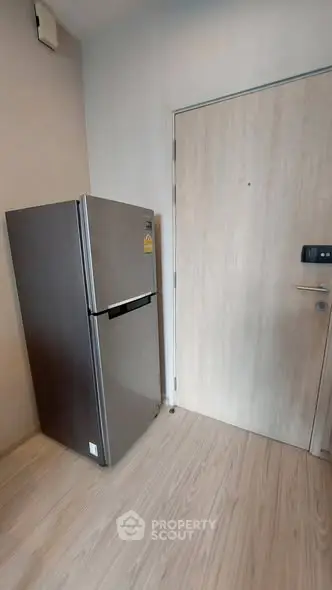 Modern kitchen corner with sleek refrigerator and wooden door, perfect for compact living spaces.