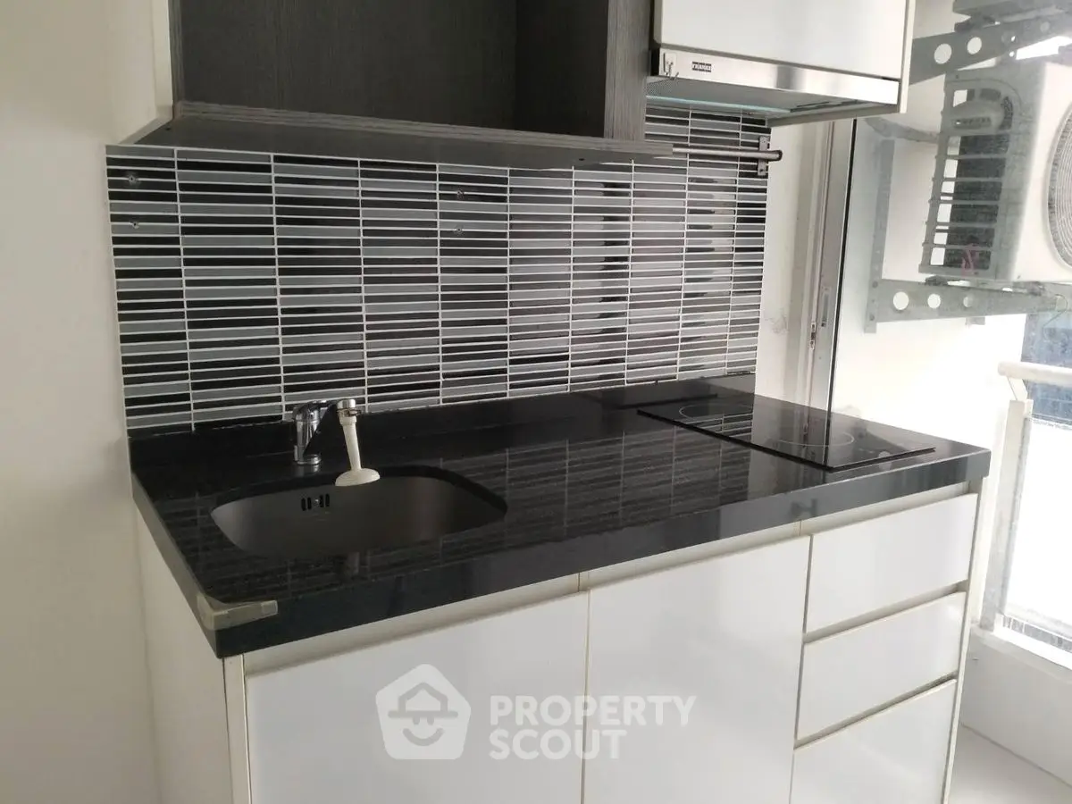 Modern kitchen with sleek black countertop and stylish backsplash in compact layout.