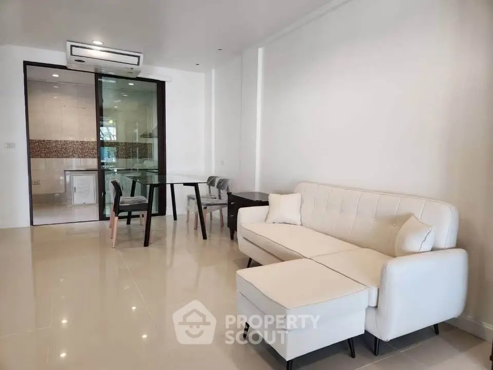 Modern living room with white sofa and glass dining table in open layout.