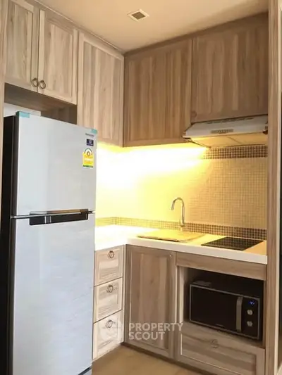 Modern kitchen with wooden cabinets, built-in microwave, and sleek refrigerator in a cozy apartment.