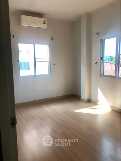 Bright empty room with wooden flooring and air conditioning, perfect for customization.