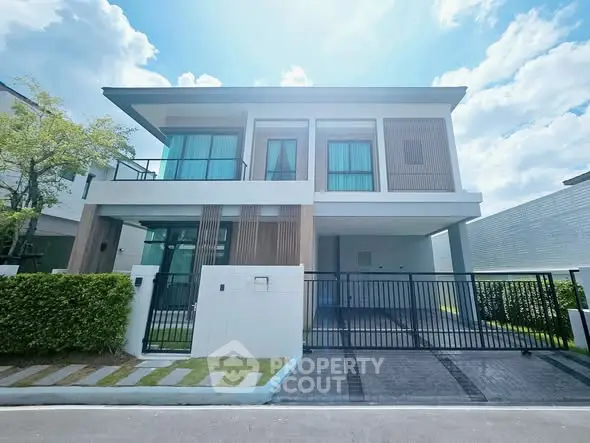 Modern two-story house with large windows and gated driveway under a bright blue sky.