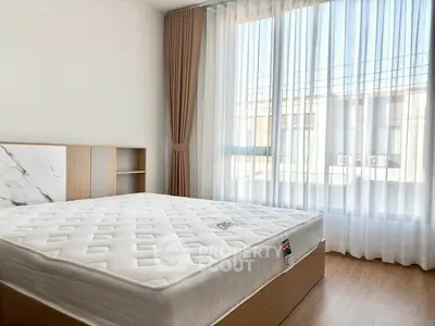 Bright bedroom with large window and modern decor, featuring a comfortable bed and elegant curtains.